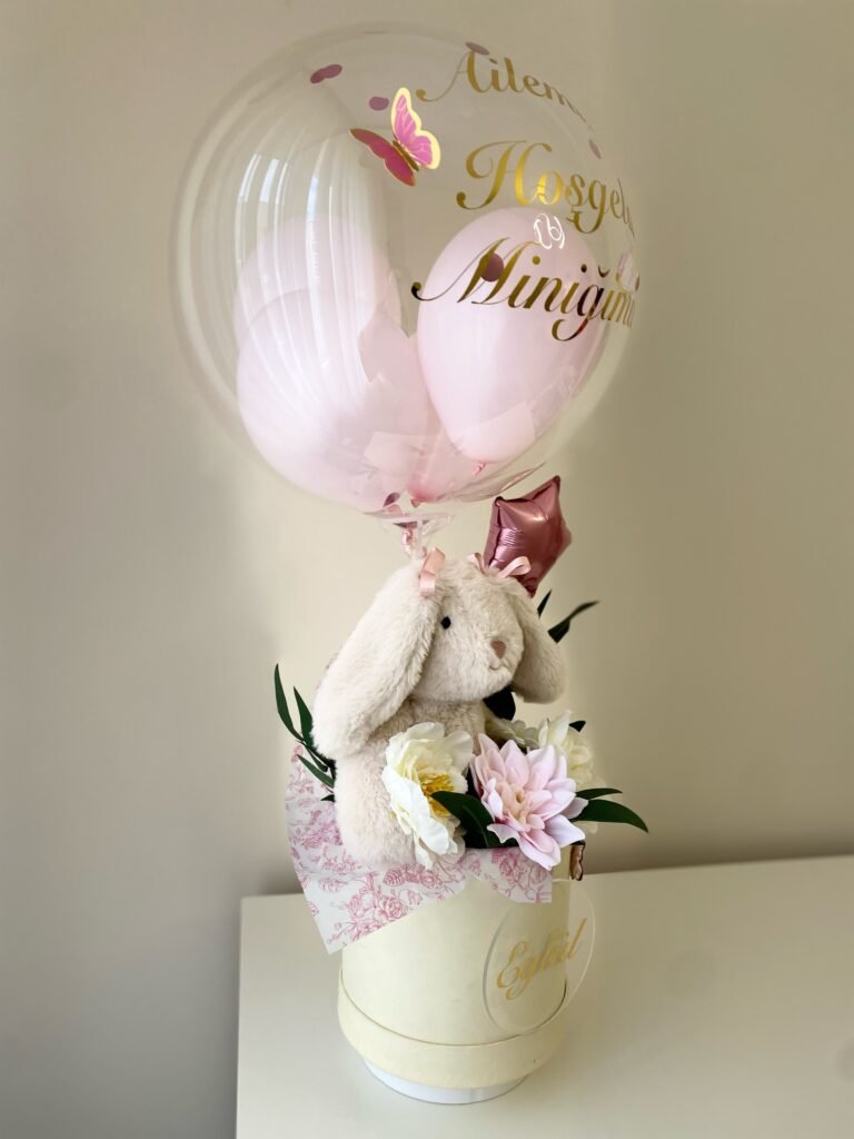 Pembe iç balonlu şeffaf bobo balonun altında peluş tavşan ve çiçekler, krem kutu yan görünümü; yenidoğan balon kutusu