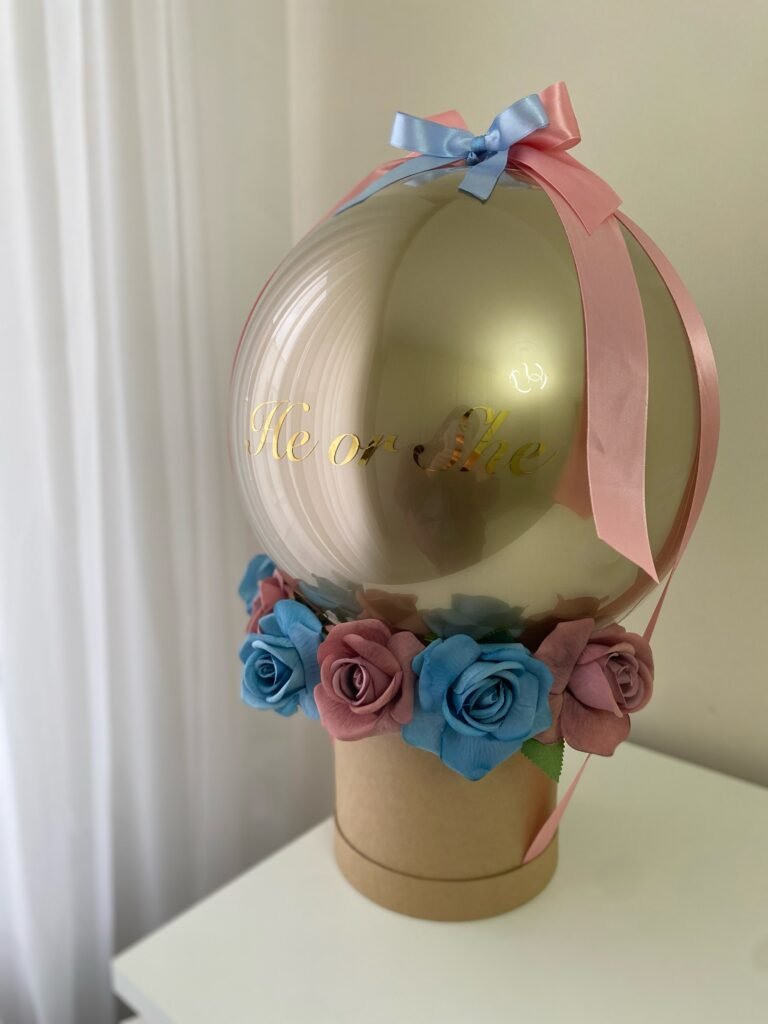 Kraft kutulu balon kutusu açılı görünüm: altın balonun tepesinde mavi fiyonk, yanlardan inen pembe saten kurdeleler