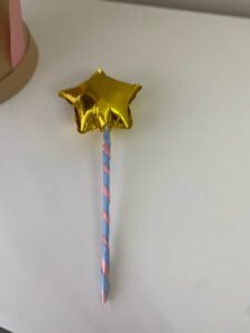 Yakın çekim: pembe ve mavi kurdeleyle sarmal biçimde sarılı çubuğa takılı altın yıldız folyo balon, masada