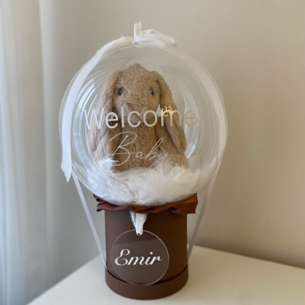 Beyaz "Welcome Baby" yazılı şeffaf balon içinde peluş tavşan ve tüyler, kahverengi kutu ve isimli pleksi; baby balon kutusu