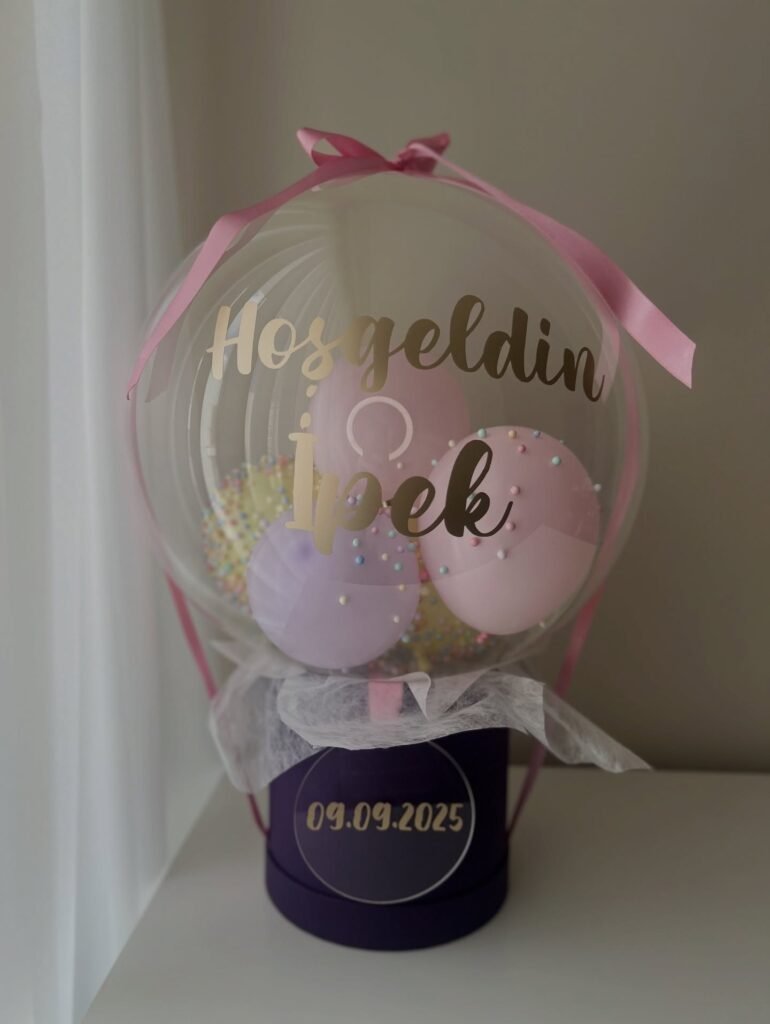 Altın "Hosgeldin" yazılı bobo balonda pembe, lila ve sarı balonlar, köpük toplar; mor kutulu pastel yenidoğan balon kutusu